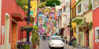 Atlixco city, Puebla state, Mexico - August 22, 2021: beautiful multi coloured street in the historical city center of Atlixco with big painted stairs, incidental cars, people during grey datime